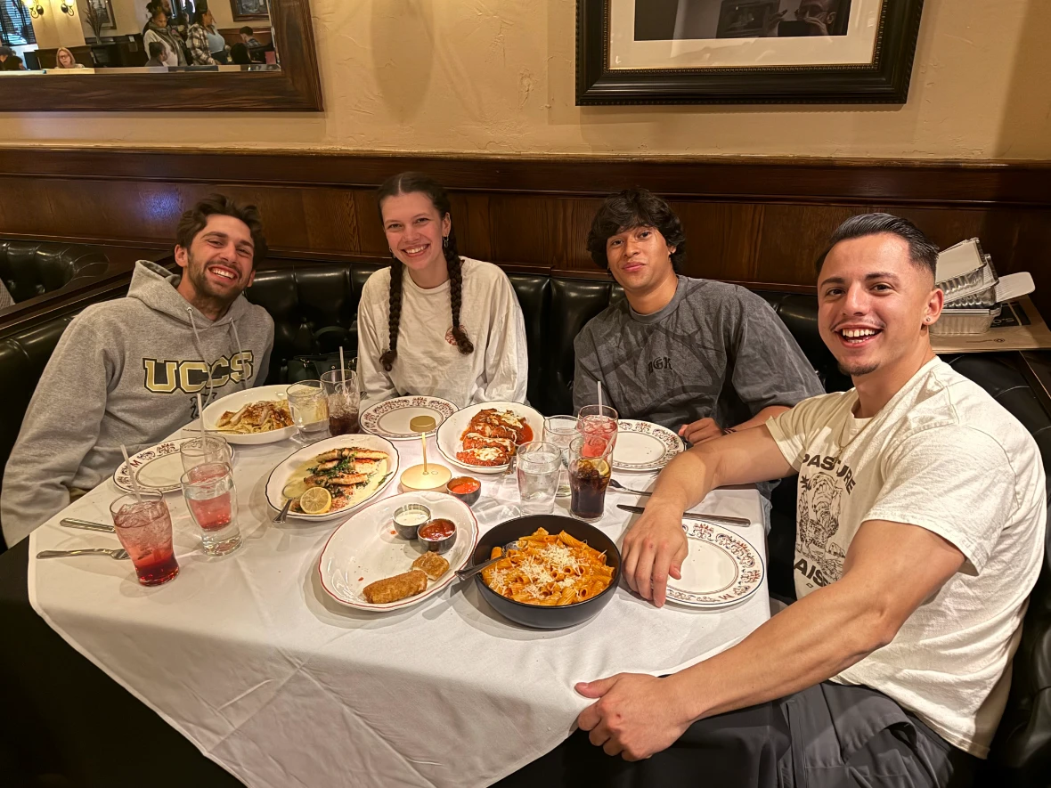Four friends smiling around a booth table covered in dishes and drinks at a restaurant.